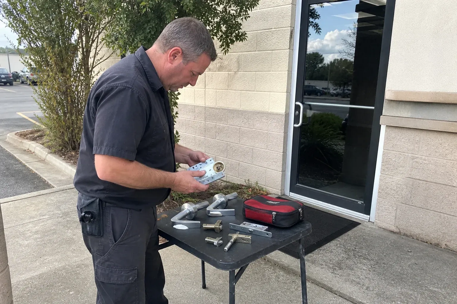 Technician examining detached commercial lock hardware on a table outside a shop entrance. — Business Lockout Service, Niagara Falls