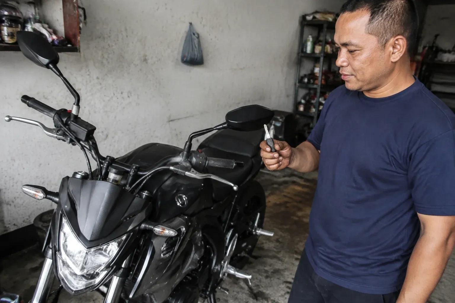Person holding a key beside a black motorcycle in a garage. — Motorcycle & Scooter Keys, Niagara Falls South